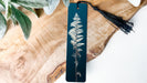 A vertical bookmark with a black tassel attached, featuring a detailed image of a fern plant on a dark blue background.