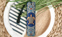 A decorative bookmark with a blue and gold design featuring a turtle, placed on a white plate with a striped pattern.