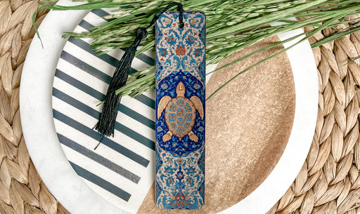 A decorative bookmark with a blue and gold design featuring a turtle, placed on a white plate with a striped pattern.