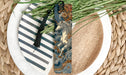 A decorative bookmark with a unicorn design is placed on a plate with a striped pattern, surrounded by green foliage.