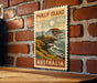 A vintage postage stamp depicting a coastal scene with a mountain, ocean, and sky, mounted on a brick wall.