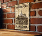 A vintage-style metal sign with a temple illustration and the text "PHNOM PENH" and "CAMBODIA" is displayed on a brick wall.