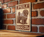 A wooden table with a wooden border, and a vintage-style stamp featuring a dog on a brick wall.