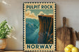 A vintage-style poster of Pulpit Rock in Norway, featuring a cliff with a river below, is displayed on a wall next to a wooden cutting board and a potted plant.