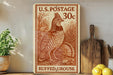 A U.S. postage stamp featuring a ruffed grouse, with a price of 30 cents, is displayed on a shelf next to a wooden cutting board and some lemons.