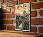 A wooden sign with a vintage-style illustration of a bridge and waterfall, mounted on a brick wall.