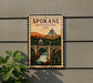 A vintage-style metal sign with a scenic illustration of a bridge, waterfall, and mountains, mounted on a wall.