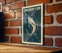 A framed image of a swordfish is displayed on a brick wall.
