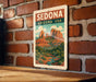 A vintage-style metal sign with the text "SEDONA ARIZONA USA" displayed on a brick wall.
