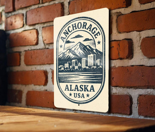 A sign with the text "ANCHORAGE ALASKA USA" and a graphic of a mountain and cityscape, mounted on a brick wall.