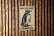 A metal sign featuring a penguin illustration is mounted on a wooden wall.