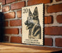 A German Shepherd dog is depicted on a German postage stamp, which is mounted on a brick wall.