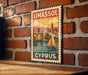 A vintage-style metal sign with a sailboat and a cityscape, mounted on a brick wall.