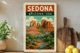 A vintage-style metal sign displaying the scenic landscape of Sedona, Arizona, USA, with a river and rock formations in the background.