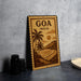 A vintage-style metal sign with the text "Goa India" and a tropical landscape illustration, placed on a gray countertop next to some black camera lenses.