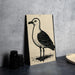 a black and white illustration of a seagull standing on one leg, placed on a gray countertop next to a stack of black camera lenses.