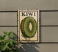 A vintage-style stamp or postcard with a kiwi fruit illustration, mounted on a wall next to a plant.