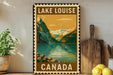 A vintage-style metal sign with the text "LAKELOUISE CANADA" displayed prominently, featuring a scenic mountain landscape with a lake and mountains in the background.