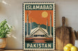 A vintage-style metal sign with the text "ISLAMABAD PAKISTAN" and an illustration of a mosque against a sunset background.