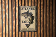 A sign for Atlantic Cod, featuring a fish illustration, is displayed on a wooden wall.