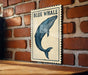 A framed illustration of a blue whale is displayed on a brick wall.