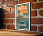 A vintage-style metal sign with the text "IBiza" and "SPAIN" printed on it, mounted on a brick wall.