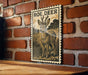 a wooden table with a framed illustration of a roe deer on it, mounted on a brick wall.