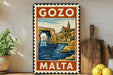 A vintage-style metal sign with the text "GOZO MALTA" and an illustration of a coastal town with a church spire, set against a backdrop of a rocky arch and a body of water.