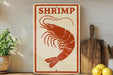 A sign with a red shrimp illustration is displayed on a shelf next to a wooden cutting board and some lemons.