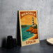 A framed poster of a lighthouse on a beach, with the text "MENORCA SPAN" printed on it, is displayed on a gray wall next to some black camera lenses.