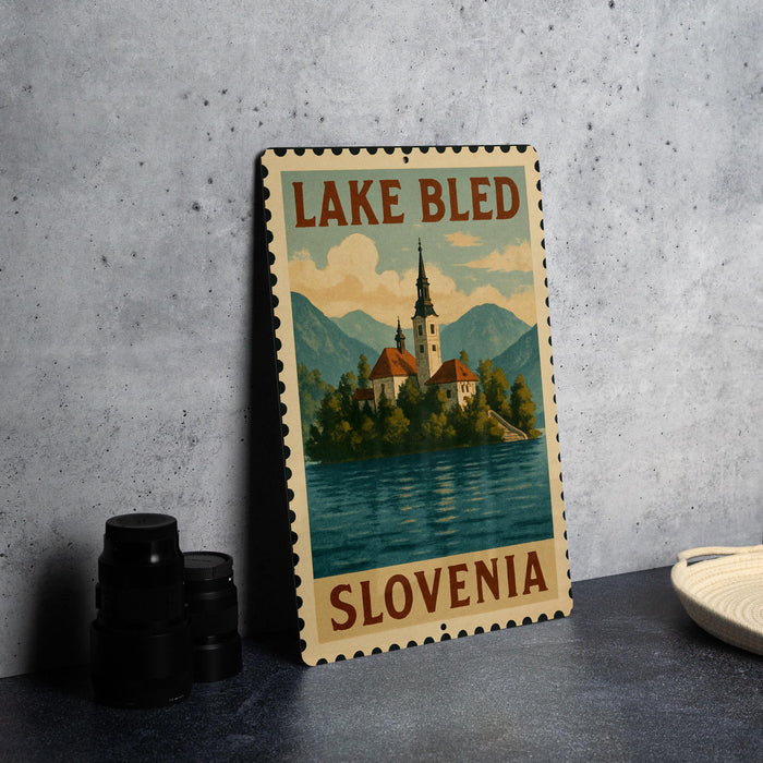 A metal sign with the text "LAKE BLEED SLOVENIA" and an illustration of a church on a lake, set against a mountainous landscape.