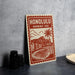 A red and white sign with the text "HONOLULU HAWAII USA" and an illustration of a beach and mountain landscape.