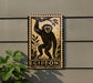 a wooden plaque with a monkey illustration on it, mounted on a wall next to a plant.