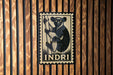 a wooden wall with a black and white illustration of a monkey on a post, and the word "INDRI" is written below the illustration.