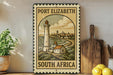 A vintage-style metal sign with a lighthouse and coastal scene, mounted on a wall next to a wooden cutting board and some potted plants.