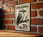 A metal sign with a black and white illustration of a bird, resembling a kookaburra, mounted on a brick wall.