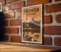 A vintage-style metal stamp depicting a scenic view of Tromsø, Norway, with a bridge and mountains in the background.