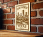 A wooden surface with a metal sign featuring a cityscape and a bridge, mounted on a brick wall.
