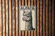 A metal sign with the word "ALPaca" on it is displayed against a wooden background.