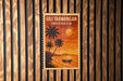 A vintage postage stamp depicting a tropical beach scene with palm trees, a boat, and a sunset over the ocean.