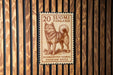 A 20 Finnish postage stamp featuring a dog, placed on a wooden wall.
