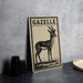 a framed illustration of a gazelle on a wall, with a stack of black camera lenses and a woven basket placed next to it.