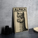 a wooden sign with an illustration of an alpaca, placed on a table next to some black camera lenses.