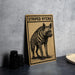 a wooden sign with a black and white illustration of a striped hyena, placed on a dark surface next to some black camera lenses.