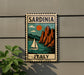 A vintage-style metal sign with a sailboat and mountains in the background, mounted on a wall.