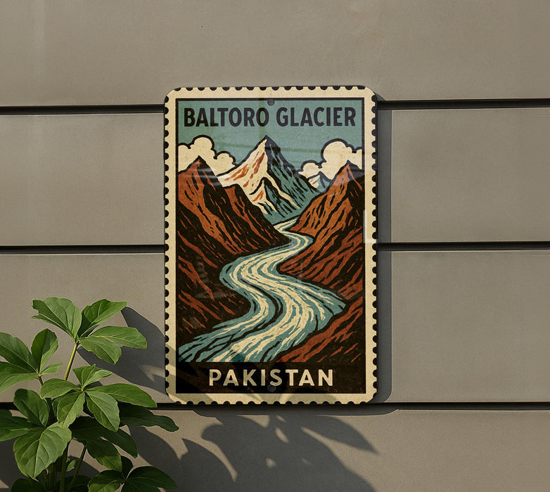 A vintage postage stamp depicting a mountain landscape with a winding river, mounted on a wall next to a plant.