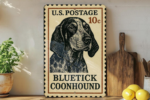 A vintage-style U.S. postage stamp featuring a blue and white spotted dog, with the text "BLUE TICK COONHOUND" printed on it. The stamp is placed on a wooden surface, with a potted plant, a wooden cutting board, and some lemons nearby.