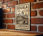 A vintage-style metal sign with the text "DOUALA CAMERON" is displayed on a brick wall.