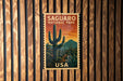 A vintage postage stamp featuring a cactus landscape and the text "SAGUARO NATIONAL PARK USA" is displayed on a wooden wall.