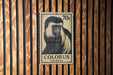 A 70 cent postage stamp featuring a colobus monkey is displayed on a wooden wall.